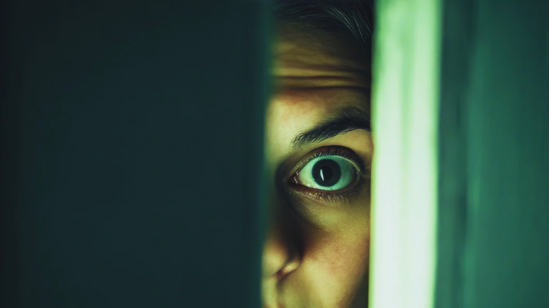 Close-up of a human eye staring through a narrow slit between dark surfaces.