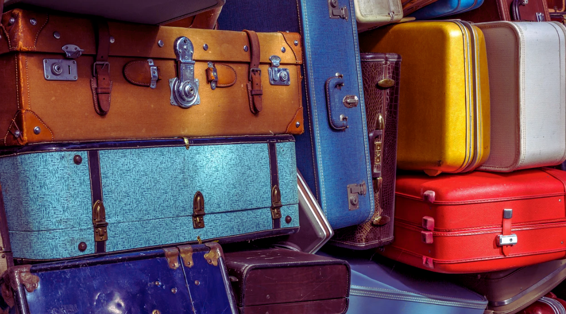 Pile of colorful vintage suitcases stacked together, showing various textures and clasps.