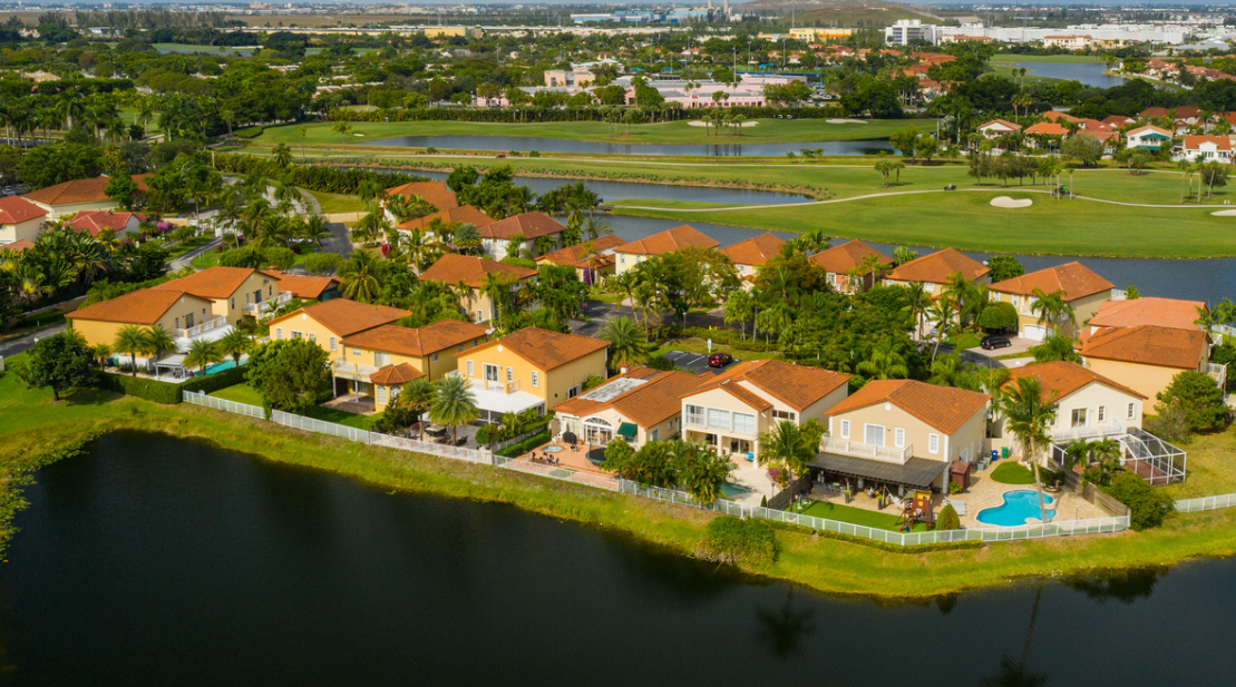 Aerial view of a suburban neighborhood with red-roofed houses, lush green lawns, a golf course, and pond—highlighting the importance of termite control and pest management to protect these beautiful homes from Asian Subterranean Termites.
